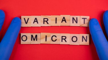 Omicron varyantı Delta 'nın yerini alır. Koronavirüsün yeni tehlikeli bir türü olan COVID-19 Omicron ortaya çıktı. Mavi eldivenler hazır. Renkli kırmızı arkaplanda omikron sözcükleri