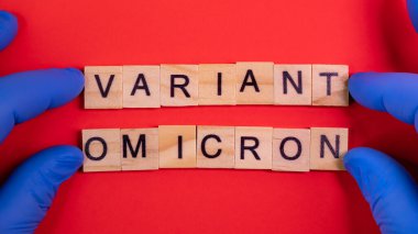 Omicron varyantı Delta 'nın yerini alır. Koronavirüsün yeni tehlikeli bir türü olan COVID-19 Omicron ortaya çıktı. Mavi eldivenler hazır. Renkli kırmızı arkaplanda omikron sözcükleri