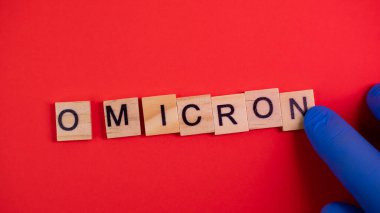 Omicron varyantı Delta 'nın yerini alır. Koronavirüsün yeni tehlikeli bir türü olan COVID-19 Omicron ortaya çıktı. Mavi eldivenler hazır. Renkli kırmızı arkaplanda omikron sözcükleri