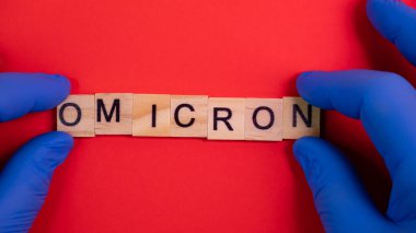 Omicron varyantı Delta 'nın yerini alır. Koronavirüsün yeni tehlikeli bir türü olan COVID-19 Omicron ortaya çıktı. Mavi eldivenler hazır. Renkli kırmızı arkaplanda omikron sözcükleri