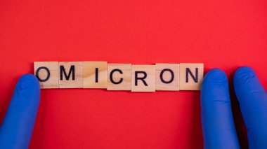 Omicron varyantı Delta 'nın yerini alır. Koronavirüsün yeni tehlikeli bir türü olan COVID-19 Omicron ortaya çıktı. Mavi eldivenler hazır. Renkli kırmızı arkaplanda omikron sözcükleri