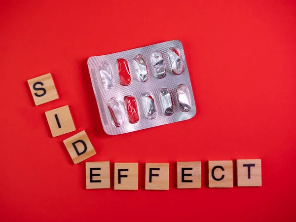 Words side effect on colored red paper texture background. Concept. Empty pill blister pack. Covid 19 illness therapy. Disease treatment side effect or toxicity. Copy space. Mock up design template