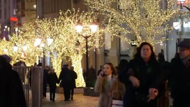 Felismerhetetlen emberek sétálnak az ünnepélyesen díszített utcán színes fényekkel.. — Stock videók