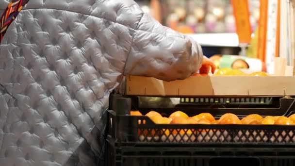 Unrecognizable elderly woman chooses persimmon in supermarket. Senior lady — Vídeos de Stock