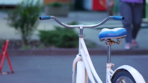 Λευκή womens ποδήλατο στέκεται στο πεζοδρόμιο και είναι δεμένο με τη συσκευή αντι-στάθμευσης — Αρχείο Βίντεο