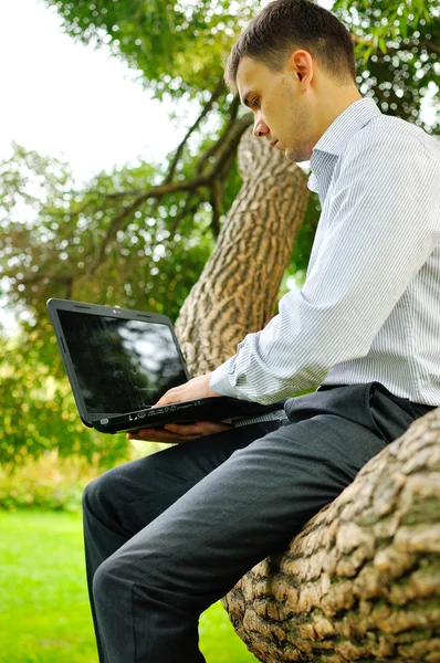 Een glimlachende man met laptop outdoor. — Stockfoto