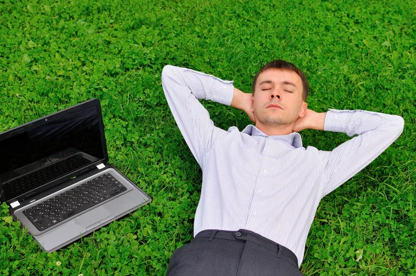 Bell'uomo sdraiato sull'erba vicino al computer portatile — Foto Stock
