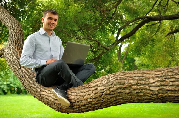 Seorang pria tersenyum menggunakan laptop outdoor. — Stok Foto
