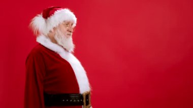 Komik Noel Baba boş yeri işaret ediyor, parmağında boşluk tutuyor ve ağzı açık şaşkın bir şekilde bakıyor, kırmızı arka planda reklamlı ürün için boş bir yer gösteriyor. Satış, İndirim, Kara Cuma.