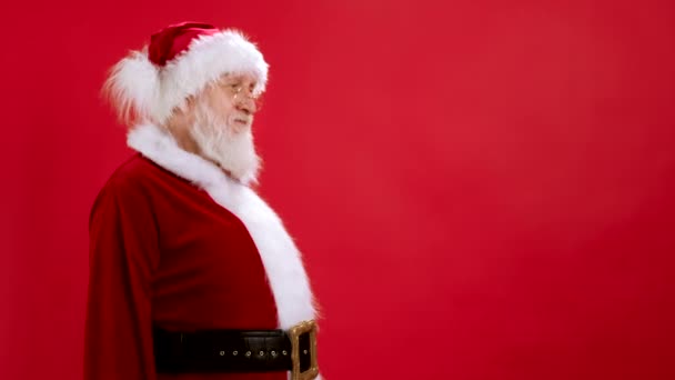 Komik Noel Baba boş yeri işaret ediyor, parmağında boşluk tutuyor ve ağzı açık şaşkın bir şekilde bakıyor, kırmızı arka planda reklamlı ürün için boş bir yer gösteriyor. Satış, İndirim, Kara Cuma. — Stok video