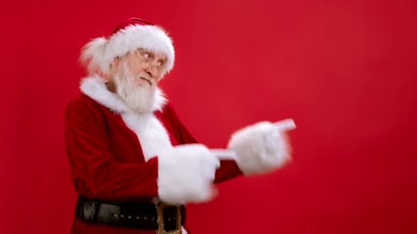 Père Noël drôle pointant vers l'espace de copie, montrant un espace de travail maquillant pour la publicité, un endroit vide pour le texte ou l'image, un contenu promotionnel. Studio Shot sur fond rouge. Vente, Remise, Black Friday. — Video