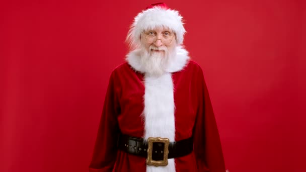 Старый бородатый Санта Клаус в рождественской шляпе в красном костюме показывает большой палец вверх, показывая большой палец вверх, палец вверх. Типа. На красном фоне студии. — стоковое видео