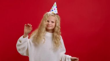 Sarışın genç zaferi kutluyor ya da kırmızı arka planda dans ederek büyük bir zafer kazanıyor. Beyaz kazaklı mutlu bir kız ve kafasında şenlikli bir koni ile sevinçle ellerini sallayarak doğum gününü kutluyor..