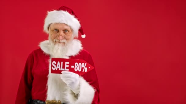 Babbo Natale tiene segno con iscrizione Vendita 80 off, punta il dito a uno spazio vuoto finto e guarda lo sconto in fotocamera e sorrisi su sfondo rosso. Grande Sconto, Natale Vacanze Vendite. — Video Stock