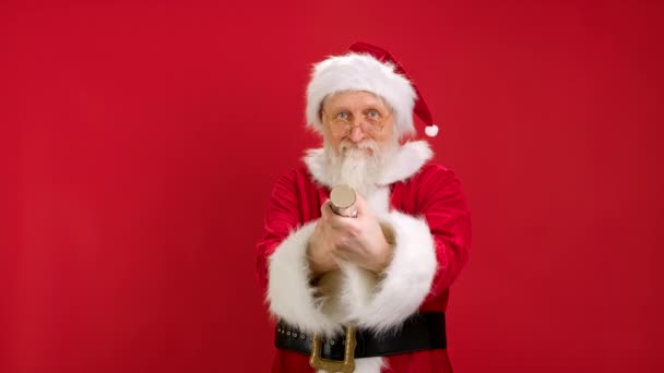 Święty Mikołaj Wysadzanie Confetti petardy Czerwone tło. Dekoracja świąteczna. Slow Motion video Portret Happy Santa Claus Próbuje dmuchnąć petardy lub otwarcie Popper w czerwonym tle. — Wideo stockowe