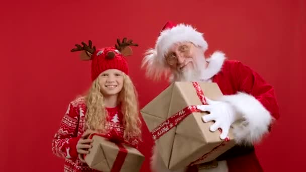 Retrato de adolescente loira e Papai Noel dançando a música de Natal com caixas de presente em suas mãos e jogando-os para a frente Regozijando-se no Natal Magia do Ano Novo em Red Beckground. — Vídeo de Stock