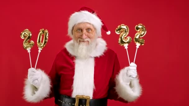 Merry Santa Claus is genieten van komende kerst met opblaasbare gouden nummers 2022 in zijn handen, Dansen en plezier hebben op rode achtergrond. Gelukkig Nieuwjaar 2022. Vrolijk Kerstfeest en Gelukkig Nieuwjaar. — Stockvideo