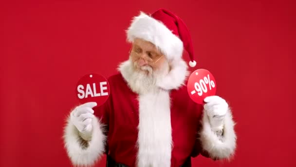 VENTE DE Noël -90 Off. Le Père Noël joyeux danse et se réjouit de la vente de Noël tenant deux bannières avec inscription VENTE et 90 off montrant des inscriptions à la caméra sur fond rouge. — Video