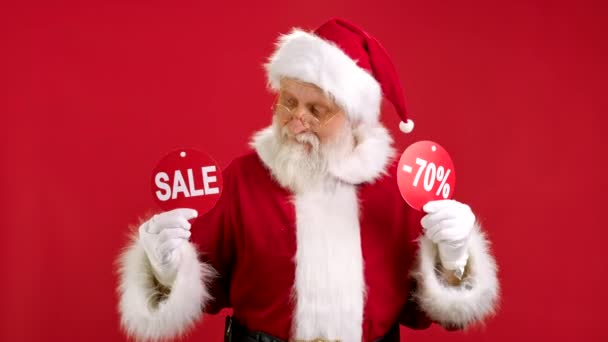 Chrismas SALE -70 Off.陽気なサンタクロースは、赤い背景にカメラへの碑文の表示をオフに碑文の販売と-70の2つのバナーを保持クリスマスセールから踊りと喜びです. — ストック動画