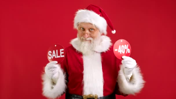 VENDITA DI Natale 40 Off. Allegro Babbo Natale sta ballando e gioioso dalla vendita di Natale che tiene due striscioni con iscrizione VENDITA e -40 Off Mostrando Iscrizioni alla fotocamera su sfondo rosso. — Video Stock