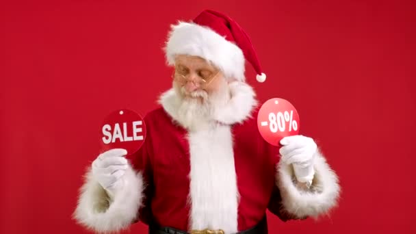 Venta de Navidad 80 Off. Alegre Santa Claus está bailando y gozoso de la venta de Navidad la celebración de dos pancartas con la venta de inscripción y 80 fuera de mostrar las inscripciones a la cámara en el fondo rojo. — Vídeos de Stock