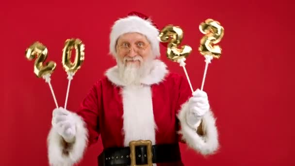Merry Santa Claus is genieten van komende kerst met opblaasbare gouden nummers 2022 in zijn handen, Dansen en plezier hebben op rode achtergrond. Gelukkig Nieuwjaar 2022. Vrolijk Kerstfeest en Gelukkig Nieuwjaar. — Stockvideo
