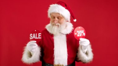 Noel indirimi -20. Neşeli Noel Baba Noel Satışı 'ndan Dans Ediyor ve Neşelidir. İthamlı iki pankart ve Kırmızı Arkaplanda Kameraya Yazıtlar Göstererek Gösteriş Yapıyor..