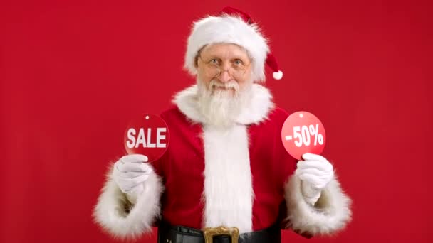 VENTE DE Noël -50 Off. Le Père Noël joyeux danse et se réjouit de la vente de Noël tenant deux bannières avec inscription VENTE et -50 off montrant des inscriptions à la caméra sur fond rouge. — Video