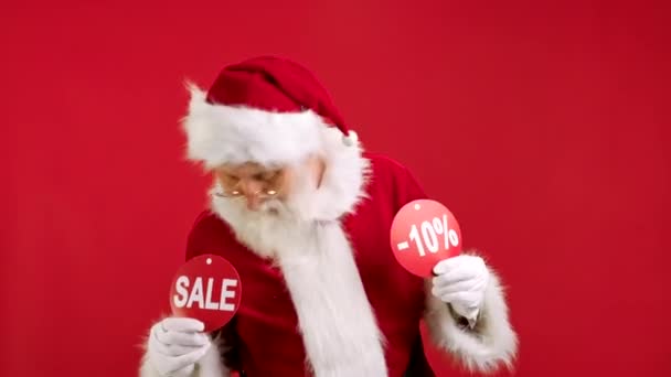 Julförsäljning -10 ledigt. Glada jultomten är dansande och glad från jul Sale håller två banderoller med inskription REA och -10 Off Visar upp inskriptioner till kameran på röd bakgrund. — Stockvideo