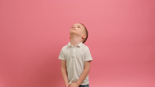 Confetti de corazones rojos cayendo de arriba a abajo. El chico atrapa confeti cayendo de corazones rojos con sus manos, divirtiéndose festejando y celebrando la victoria sobre fondo rosa. Concepto de Día de San Valentín. — Vídeos de Stock