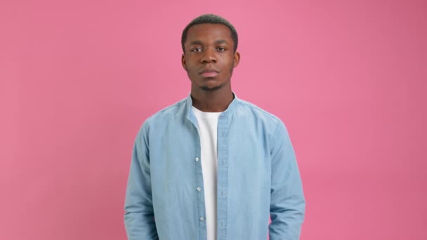 Serious African American man in white T-shirt and denim shirt advertises big discount and sales on Black Friday, holding red sign with word SALE on pink background. SALE message with place for text. — стокове відео