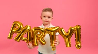 Mutlu, sarışın, beyaz çocuk ellerinde altın harflerle dans etmekten mutluluk duyar. Pembe arka planda parti yazılıdır. Çocuk altın balon harflerle parti yazısını gösteriyor..