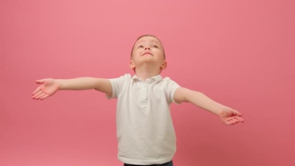 Cute caucasian blond boy catches red hearts falling from above with his hands and enjoys holiday on pink background. Concept of birthday greetings, Valentines day, victory celebration, confetti party. — стокове відео