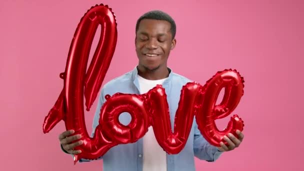 Афроамериканская подросток держит в руках красный надувной гелиевый шар с надписью ЛЮБОВЬ улыбается и счастливо танцует, празднуя День Святого Валентина или День матери. Концепция поздравления с днем любви. — стоковое видео