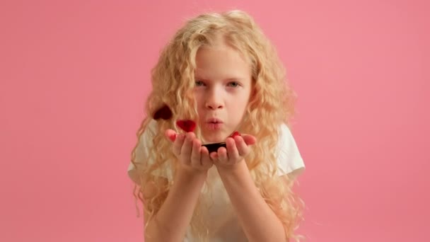 Portrait smiling young girl in purple trendy hoodie blowing red confetti in shape of heart out of her hands, celebrating Valentines Day. Slow motion video Cheerful girl congratulates on Mothers Day. — Vídeo de Stock