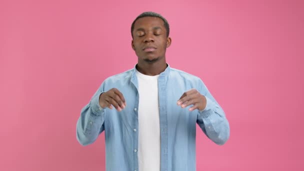 Retrato espiritual tranquilo afroamericano de 20 años, vestido con camisa de mezclilla, con las manos separadas en yoga om aum gesto, meditando, tratando de calmarse, aislado sobre un fondo rosa simple. — Vídeo de stock