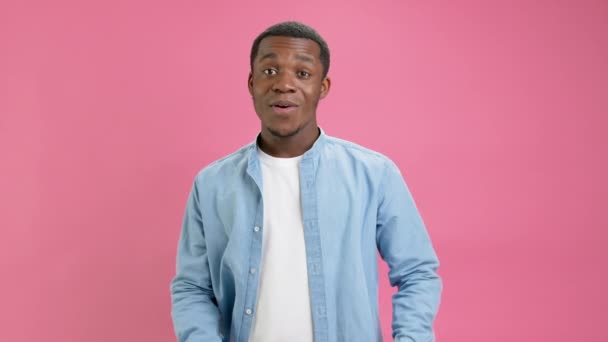 Smiling black guy, African American 20 years in denim shirt, white T-shirt, looks approvingly at camera, showing thumbs up, like and approval in social networks or video, on pink studio background. — 图库视频影像