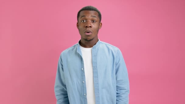 Emotional black African American man in denim shirt and white T-shirt looking shocked, surprised, wow, shows his hands, brain explosion head isolated on pink studio background. Concept brain overload. — Stock video