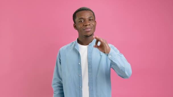 Excited funny 18 year old young bearded African American, dressed in denim shirt, looks at camera, speaks and gestures showing gesture OK posing in isolation on pink background in studio. — 图库视频影像