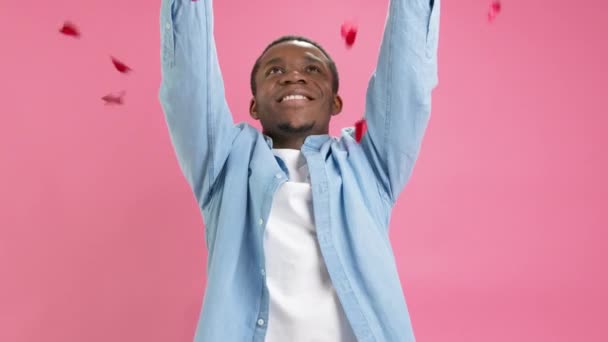 Slow motion portrait happy smiling African-American man celebrating Valentines Day or mothers Day throws up red candy in form of hearts and rows hearts with his hands smiling looks at camera. — стокове відео
