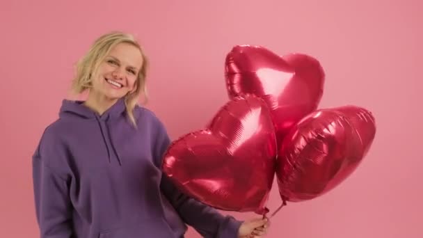 Portrait cheerful smiling woman is enjoying Mothers Day or Valentines Day dancing with red gel balls in shape of heart on pink background. Concept of love, romance and happy family. — Stock videók