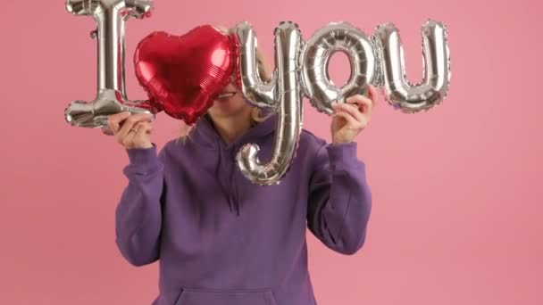Porträt in Zeitlupe einer glücklichen 30-jährigen Frau, die lächelt und tanzt, einen Heliumballon mit der Aufschrift I LOVE YOU in der Hand hält, sich hinter Luftballons versteckt und zum Muttertag oder Valentinstag gratuliert. — Stockvideo