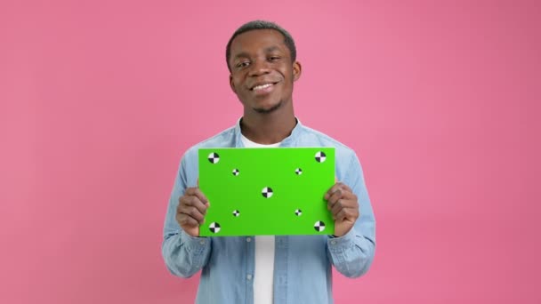 African American Man Holding Green Screen Banner Tracking Points for Copy Space. Blank Green Screen Board. Shows an Approving Thumbs-up Gesture With Space for Text or Advertising on pink Background. — Video