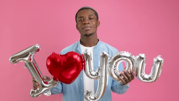 Usmívající se afroamerický teenager volá po lásce nebo vyznává svou lásku k bližnímu, drží slovo, že tě miluji z heliového balónku v jeho rukou, blahopřeje ke Dni matek nebo Valentýnu. — Stock video