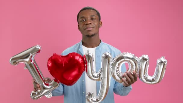 Sonriente adolescente afroamericano pide amor o confiesa su amor a su ser querido, sostiene la palabra Te amo desde el globo de helio en sus manos, felicita el Día de la Madre o el Día de San Valentín. — Vídeos de Stock