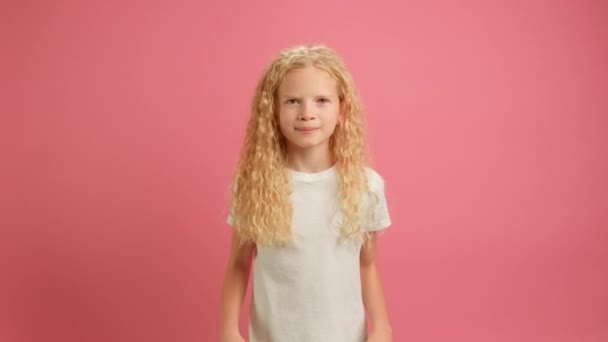 Αργή κίνηση πορτρέτο ξανθιά ευτυχισμένη καυκάσιος έφηβος κορίτσι σε λευκό T-shirt, χαμογελώντας χαρούμενα και πηδώντας από χαρά σαν μαϊμού, κουνώντας τα χέρια της. Ευτυχισμένο παιδί πηδά συναισθηματικά σε ροζ φόντο στούντιο — Αρχείο Βίντεο