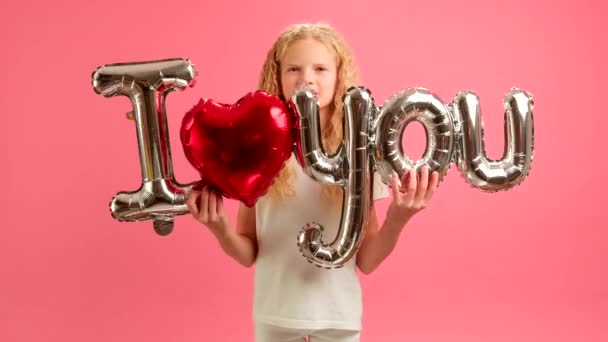 Szőke tinédzser lány bevallja szerelmét a családjának vagy anyjának az ünnepi műsorokban, felirattal, hogy szeretlek rózsaszín háttérrel. Gratulálunk a lánytól az Anyák Napján vagy Valentin napon. — Stock videók