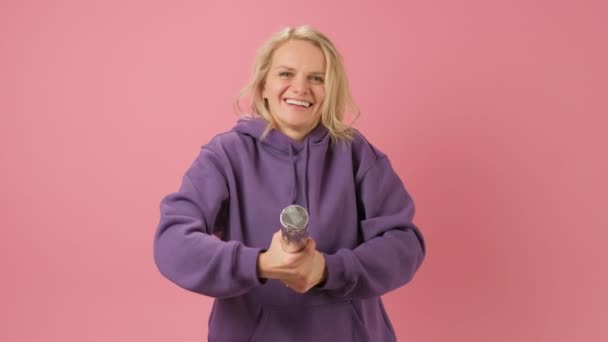 Blond woman celebrates victory or significant event, explodes firecracker with red hearts and rejoices in birthday on pink background. Slow motion Holidays with confetti on Valentines Day, Mother Day. — Stock Video