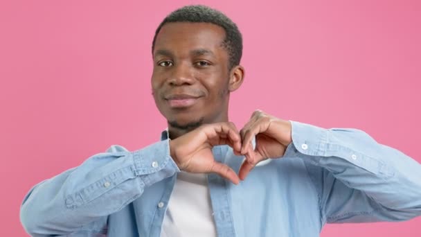 Ritratto di spensierato afroamericano allegro adolescente in camicia blu che soffia corietti a forma di cuore rosso, fare con le dita a forma di cuore, godendo di compleanno o San Valentino o giorno delle madri. — Video Stock