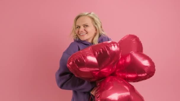 Portrait of cheerful smiling woman enjoying Mothers Day or Valentines Day hides her face with red gel balls in shape of heart on pink background, peeks out of red hearts. love concept, happy family. — Vídeo de Stock